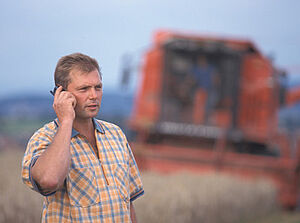 Ein Mann auf einem Feld vor einem Mähdrescher telefoniert.