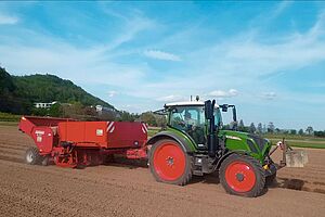 Traktor mit rotem Anhänger bei der Kartoffelpflanzung