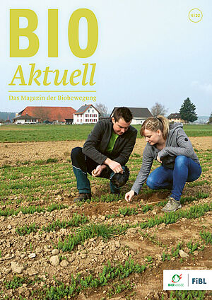 Titelseite Bioaktuell 4|2022: Zwei Personen auf dem Lein-Feld, im Hintergrund der Betrieb.