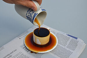 Kaffekanne giesst Kaffee in überlaufende Tasse
