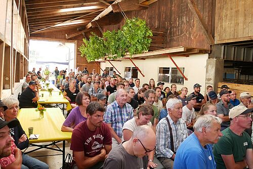 Grosse Menschenmenge in einem landwirtschaftlichen Gebäude. 