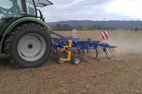 Traktor zieht einen Flachgrubber über einen Acker.