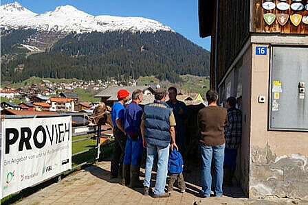 Eine Gruppe von Personen vor einem Stall, am Geländer eine Blache mit der Aufschrift "Provieh"