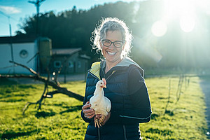 Frau hält weisses Huhn in den Armen.