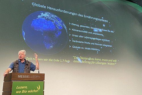 Ein Mann referiert vor einer Powerpoint-Präsentation.