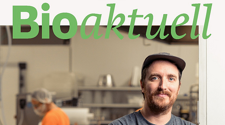 Titelseite Bioaktuell 10|25: Ein Mann schaut mit verschränkten Armen in die Kamera, im Hintergrund ist eine Person an einer Anlage am Arbeiten.