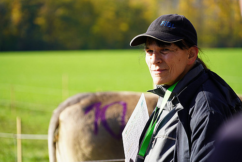 Eine Frau mit einem Baseballcap, dahinter eine halb verdeckte Kuh.