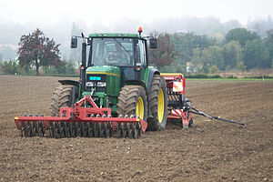 Traktor mit Walze an der Front und Sämaschine am Heck im Einsatz