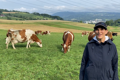 Eine Frau steht mit Baseballcap auf einer Kuhweide. 