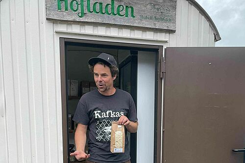 Ein Mann steht im Türrahmen und hält ein Tüte mit Haferflocken in der Hand