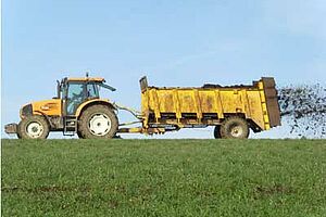 Traktor und Mistzetter beim Ausbringen von Mist auf einem Acker.