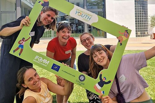 Fünf junge Frauen halten einen grossen Fotorahmen mit der Aufschrift Organics Europe Youth Event und lachen in die Kamera.
