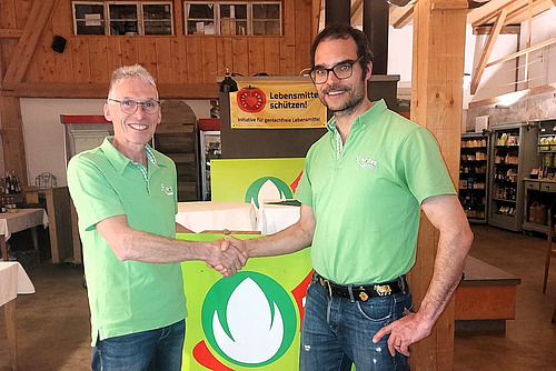 Zwei Männer in grünen T-Shirts schütteln sich die Hand vor einem Bio Suisse-Logo.