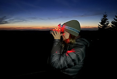 Alice Dind schaut mit einem rot leuchtenden Wärmebildfernglas in die Ferne.