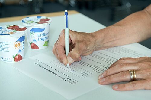 Zwei Hände, die neben zwei Joghurts einen Fragebogen ausfüllen.
