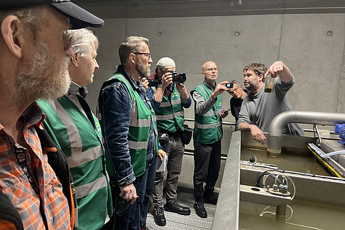 Eine Menschengruppe in grünen Gilets mit einem Instruktor, der ein Glas mit Wasser in der Hand hält. 