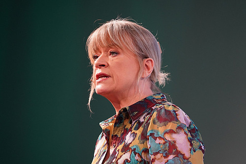 Eine Frau moderiert vor einer grünen Wand.