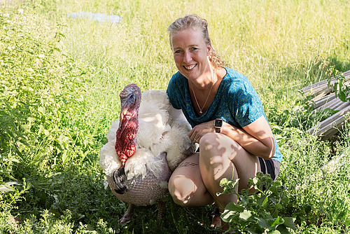 Eine Frau in kurzen Hosen und grünem T-Shirt posiert mit einem Truthahn. 