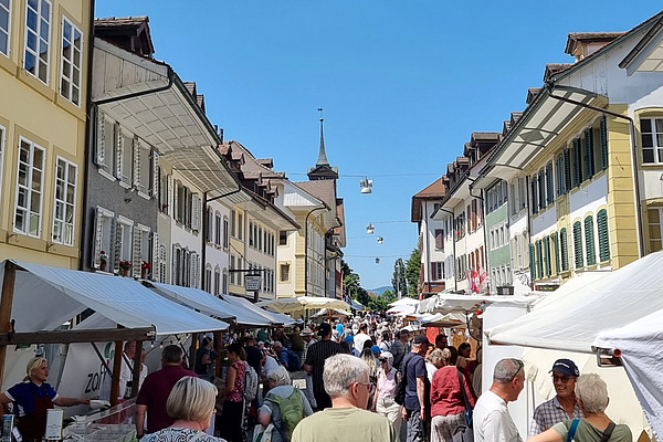 Blick in eine Altstadt-Gasse mit Markt, gut besucht von zahlreichen Menschen. 