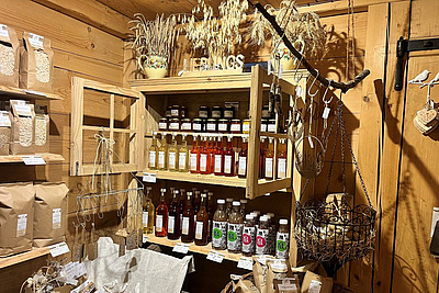 Regale gefüllt mit Konfitüren, Flaschen und verpackten Hofprodukten in einem Hofladen. 