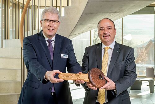 Zwei Männer im neuen FiBL-Gebäude halten gemeinsam einen Holzschlüssel.