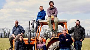 Das Team posiert auf einem roten Traktor auf einem Feld