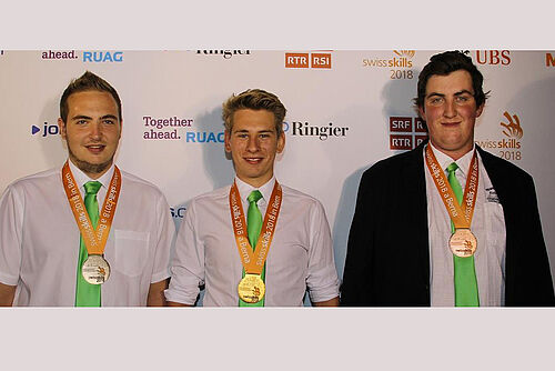 drei junge Männer mit Medaillen um den Hals