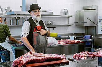 Ein Mann steht vor einer Edelstahlanrichte mit einem grossen Stück Fleisch. 