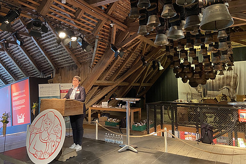 Eine Frau referiert vor Publikum in einer alten Scheune. 