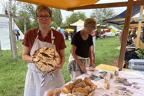 Eine Frau hält ein Brot an einem Marktstand.