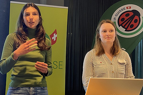 Zwei Frauen vor einer Wand mit zwei Logos.