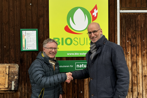 Zwei Menschen schütteln sich vor der Bio Suisse-Hoftafel die Hand.
