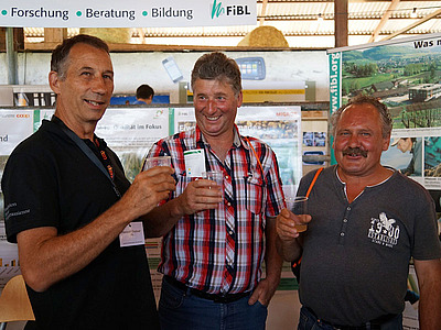 drei Männer heben beim FiBL-Stand ihr Mostglas