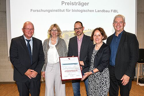 Drei Herren und zwei Damen stehen vor einer Leinwand und halten ein Schild mit dem Titel Anerkennungspreis in den Händen