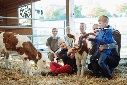 Familie mit vier Kindern sitzt im Stall, neben ihnen ein Kalb.