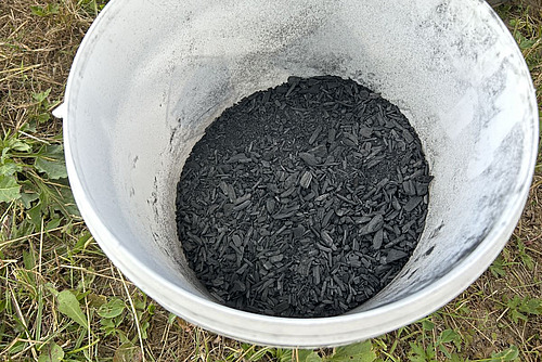 Weisser Plastikeimer gefüllt mit schwarzer Kohle.