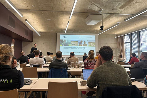 Eine Person präsentiert den Teilnehmenden in einem Tagungssaal eine Präsentation über Nachhaltigkeitsbewertungen.