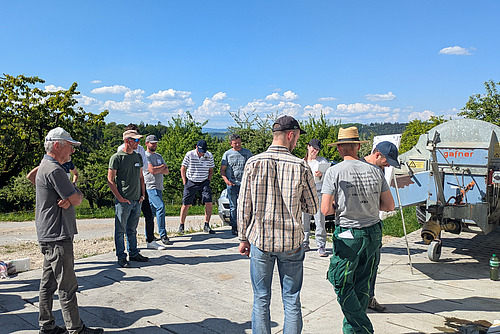 Eine Gruppe von Teilnehmer*innen steht bei schönstem Wetter draussen in einem Kreis.