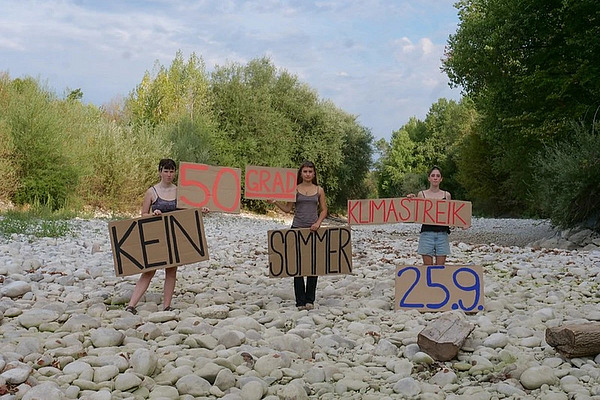 Klimastreik-Aktion in einem ausgetrockneten Flussbett: Drei Personen halten Schilder mit den Botschaften „Kein Sommer“, „50 Grad“, „Klimastreik“ und „25.9.“ und verweisen damit auf die Folgen des Klimawandels wie Hitze und Wasserknappheit.