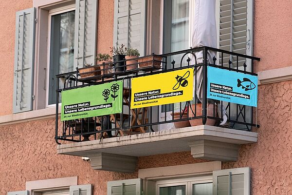 Ein Balkon mit drei Fahnen, die für die Biodiversitäts-Initiative werben.