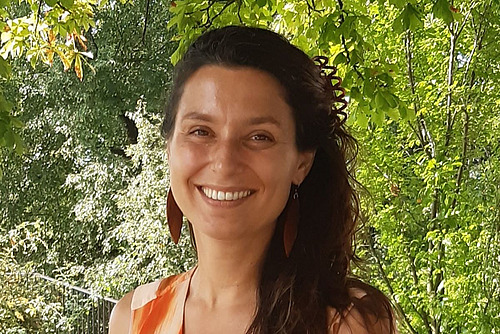 Portrait einer Frau mit braunen langen Haaren vor einem grünen Hintergrund.