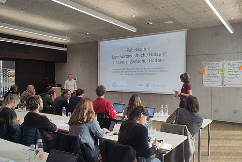 Tagungsraum mit Zuhörenden, die einer Präsentation über Paludikultur folgen.