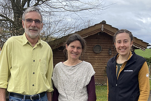 Drei Personen posieren vor einem hölzernen Gartenhäuschen.