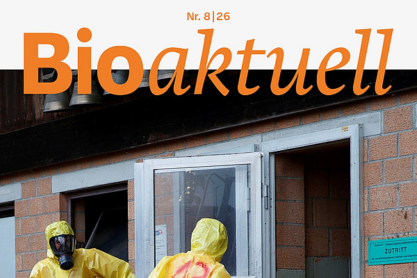 Titelseite Bioaktuell 8|26: Drei Menschen in Schutzanzügen und Atemmasken beim Eingang zu einem Stall.