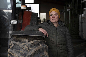 Junge Frau lehnt mit dem Arm an einen Traktor.