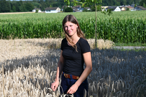 Eine braunhaarige Frau steht in einem Getreidefeld.
