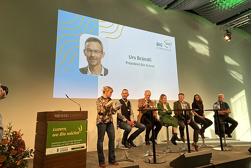 Ein Podium mit sieben Teilnehmenden auf einer Bühne.