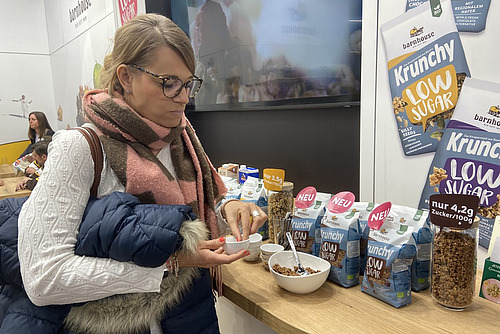 Eine Frau mit einer Handvoll trockenem Knuspermüesli degustiert in kleinen Portionen an einem Messestand. 