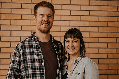 Ein Mann und eine Frau posieren vor einer Backsteinmauer. 