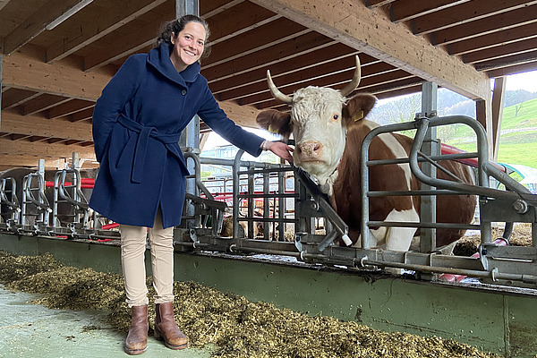 Eine Frau mit einer Kuh am Fressgitter in einem Laufstall.